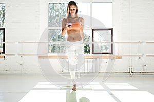 Woman training and stretching muscles in white gym and hold mobile phone in hand and counts calories in application on smar