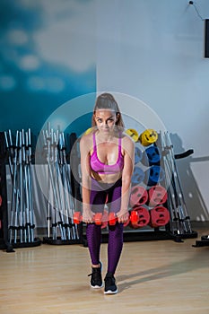 Woman trains in the gym with dumbbells and demonstrates athletic shape