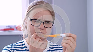 A woman in transparent glasses smiles and looking at a temperature thermometer
