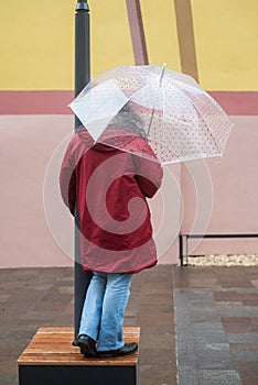 Woman with transparent umbrella and red coat standing in cobbles place