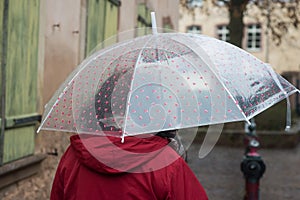 Woman with transparent umbrella and red coat walking in cobbles street