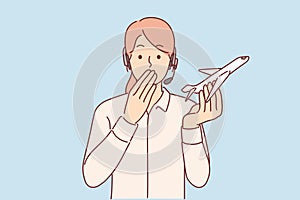 Woman travel agent holds airplane and covers mouth, feeling shocked by information about plane crash