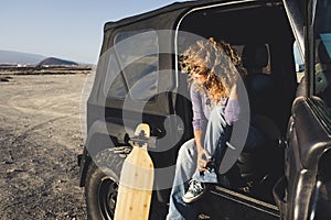 Woman travel alone with black car and long board table on the wild road- journey and adventure lifestyle female people sitting