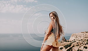 Woman travel sea. Happy tourist taking picture outdoors for memories. Woman traveler looks at the edge of the cliff on