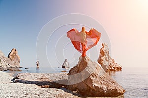 Woman travel sea. Young Happy woman in a long red dress posing on a beach near the sea on background of volcanic rocks