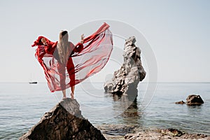 Woman travel sea. Young Happy woman in a long red dress posing on a beach near the sea on background of volcanic rocks