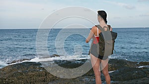 Woman traveler admiring sea view and making photo on the beach using smartphone