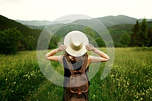 Woman traveler with backpack holding hat and looking at amazing