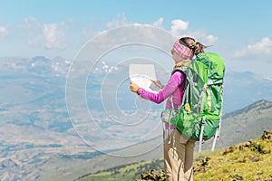 Woman traveler with a backpack and a map on the background of the Pyrenees mountains. Hiking and adventure concept