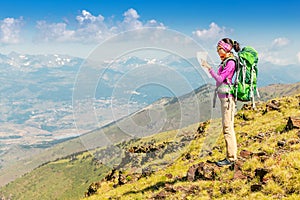 Woman traveler with a backpack and a map on the background of the Pyrenees mountains. Hiking and adventure concept