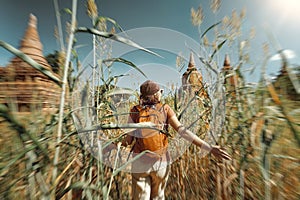 woman traveler with a backpack run through field to ancient stupas.