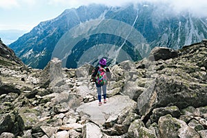 Woman traveler with backpack tracking sticks top mountain