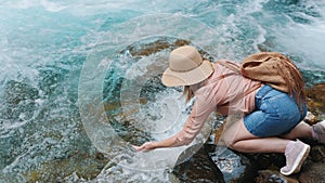 A woman traveler bent down to drink water from a river