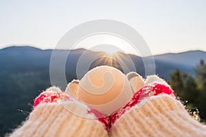 Woman traveler in christmas gloves holding snowball on a background of mountains with sunbeams. Winter travelling concept.