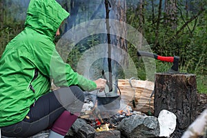 Woman traveler cooking food in kettle on fire in forest