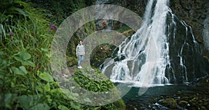 Woman traveler enjoying waterfall in the highlands of Austria. Traveling in the mountains, adventure and trip concept.