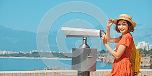 Woman traveler in hat looking through tourist binoculars at a tropical resort