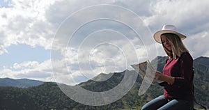 Woman traveler hiker sitting on top of rocky mountains learning route on map.