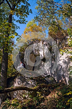 Woman traveler hiking on a large boulder, resting among the wild nature of the autumn forest in the day. Travel and nature.