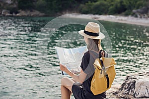 Young woman traveler with backpack holding map by the sea. Travel, tourism, summer holidays concept.