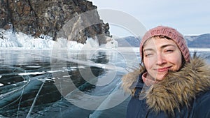 Woman traveler makes a selfie against the rock and Baikal ice. Smiling traveler in winter clothes
