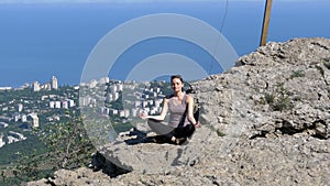 Woman traveler meditates in mountains, sitting on top of a cliff in the lotus position