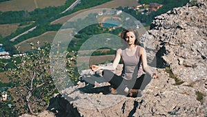 Woman traveler meditates in mountains, sitting on top of a cliff in the lotus position