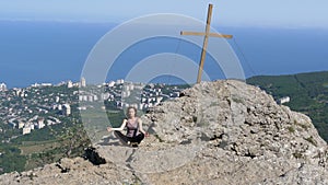 Woman traveler meditates in mountains, sitting on top of a cliff in the lotus position