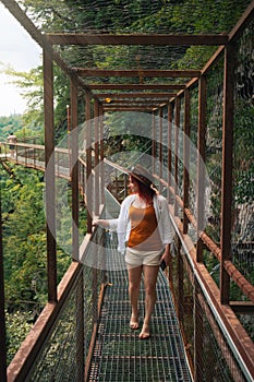 Woman traveler in Okatse Canyon in Georgia, standing on hanging metal pedestrian pathway trail above deep precipice. Leather hat.