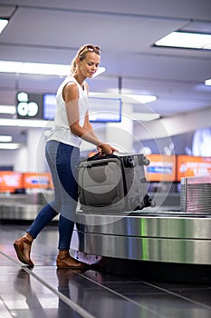 Woman traveler picking up suitcase from baggage claim