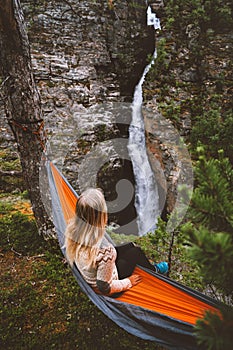 Woman traveler relaxing in hammock with waterfall view in Norway travel lifestyle outdoor summer camping