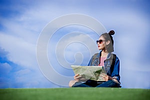 Woman traveler sit down on green grass and looking a map on the