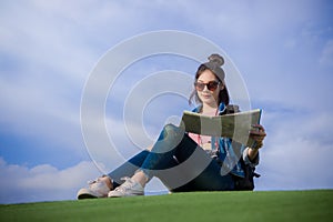 Woman traveler sit down on green grass and looking a map on the