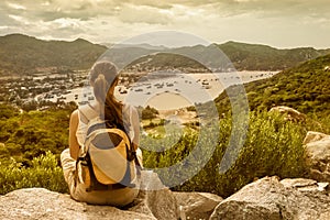 Woman traveler sits and looks at the edge of the cliff on the s