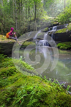 Woman traveler sitting on a rock in front of a waterfall Tham Yai Waterfall Phu Kradueng