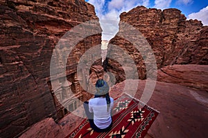 Woman traveler sitting on viewpoint in Petra ancient city looking at Treasury Al-khazneh