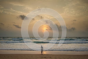 Woman traveler standing in the distance on the beach and looking at the sunset