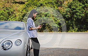 Woman traveler standing next to car trying to get signal on mobile phone.