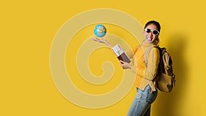 Woman traveler with suitcase, holding ball globe in the hand with passport and ticket on Yellow background. Portrait of smiling