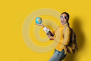 Woman traveler with suitcase, holding ball globe in the hand with passport and ticket on Yellow background. Portrait of smiling