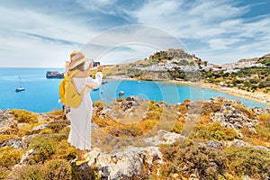 Woman traveler taking photo of her smartphone scenic landscape of a famous tourist attraction on Rhodes Island - Lindos town