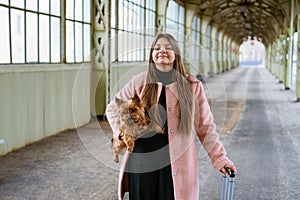 Woman traveler tourist walks with luggage and dog at train station in pink