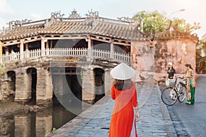 Woman traveler wearing Ao Dai Vietnamese dress sightseeing at Japanese covered bridge in Hoi An town, Vietnam. landmark and