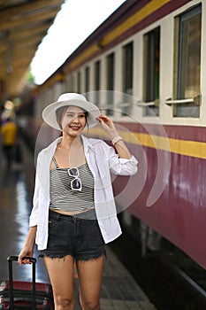 Woman traveler wearing white hat walking with her suitcase at platform.