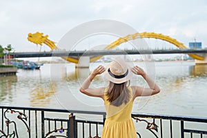 Woman Traveler with yellow dress visiting in Da Nang. Tourist sightseeing the river view with Dragon bridge at love lock bridge.