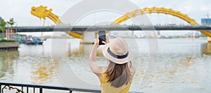 Woman Traveler with yellow dress visiting in Da Nang. Tourist sightseeing the river view with Dragon bridge at love lock bridge.