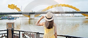 Woman Traveler with yellow dress visiting in Da Nang. Tourist sightseeing the river view with Dragon bridge at love lock bridge.