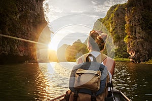 Woman traveling by boat enjoying sunset among of karst mountains