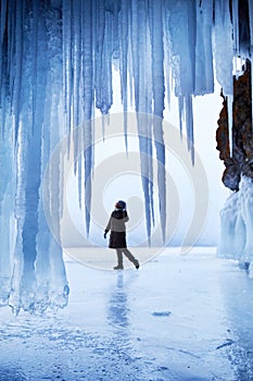 A woman traveling on the frozen Lake Baikal in winter. View from an ice cave with huge icicles.