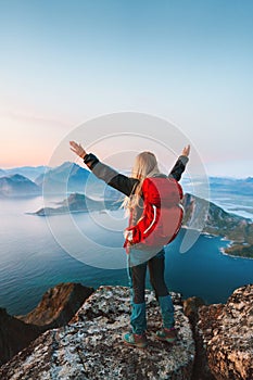 Woman traveling in Norway tourist on mountain cliff edge in Lofoten islands girl raised hands with backpack hiking outdoor